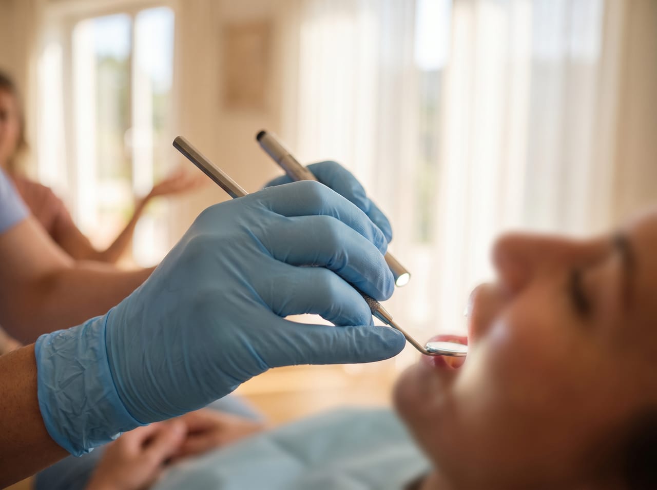 A dentist in gloves examining a patient with a mirror in a cool-lit treatment room